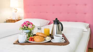 A neatly made breakfast tray on a bed with a pink headboard, including croissants, strawberries, a coffee cup, and a juice glass.