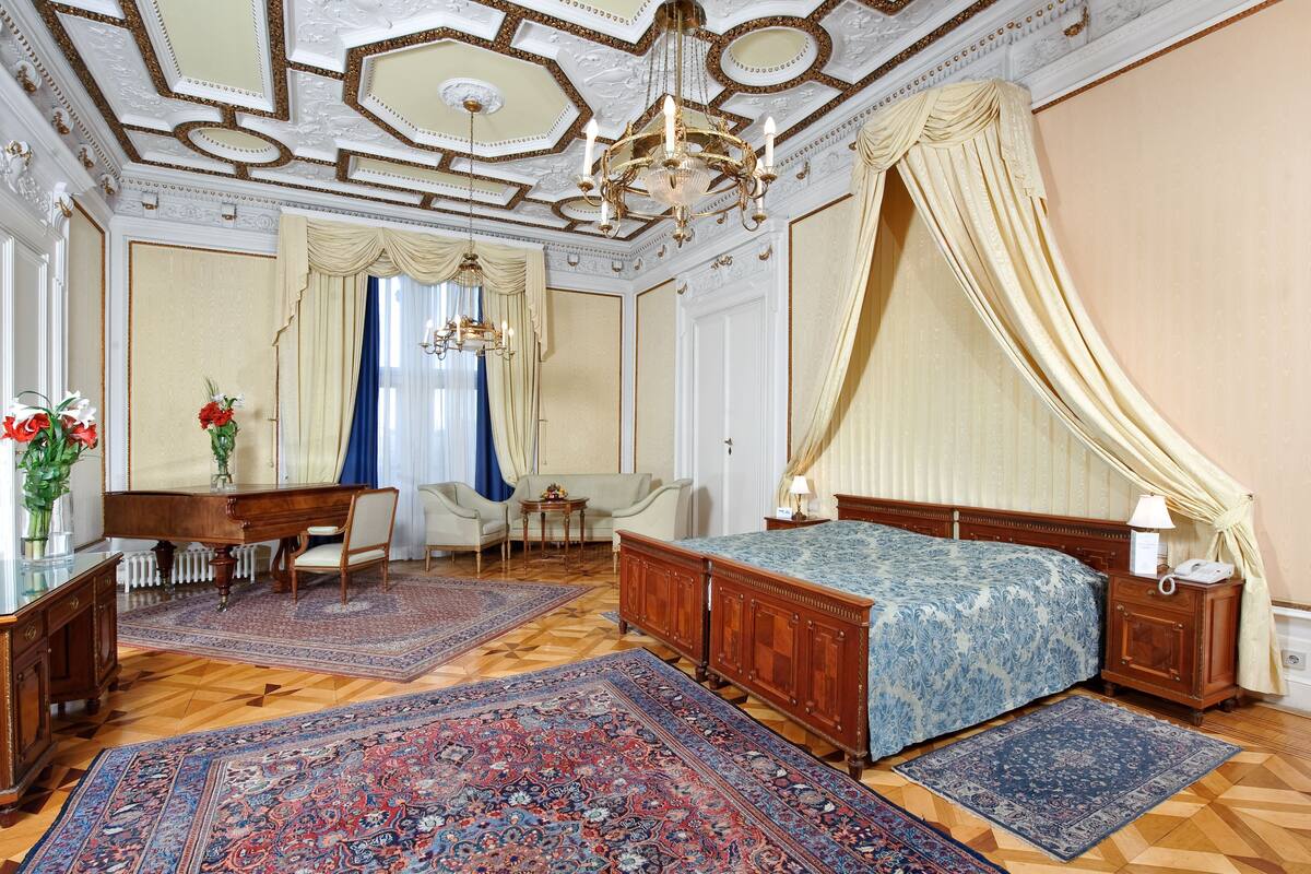 Een ruime slaapkamer met een groot bed, een houten dressoir, een bureau met stoel en een kroonluchter.