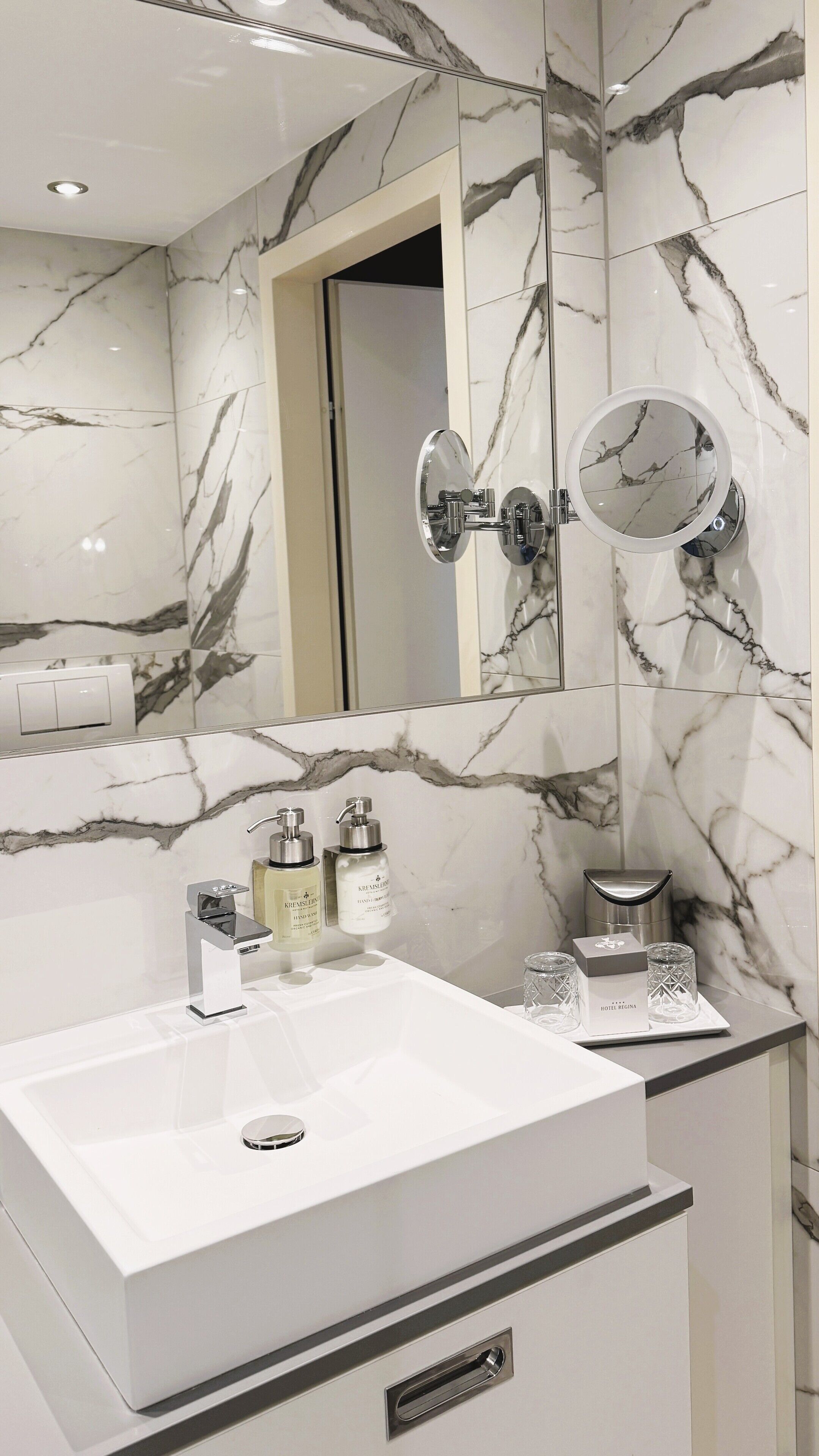 A modern bathroom with a white marble sink, two mirrors, and a handheld showerhead.