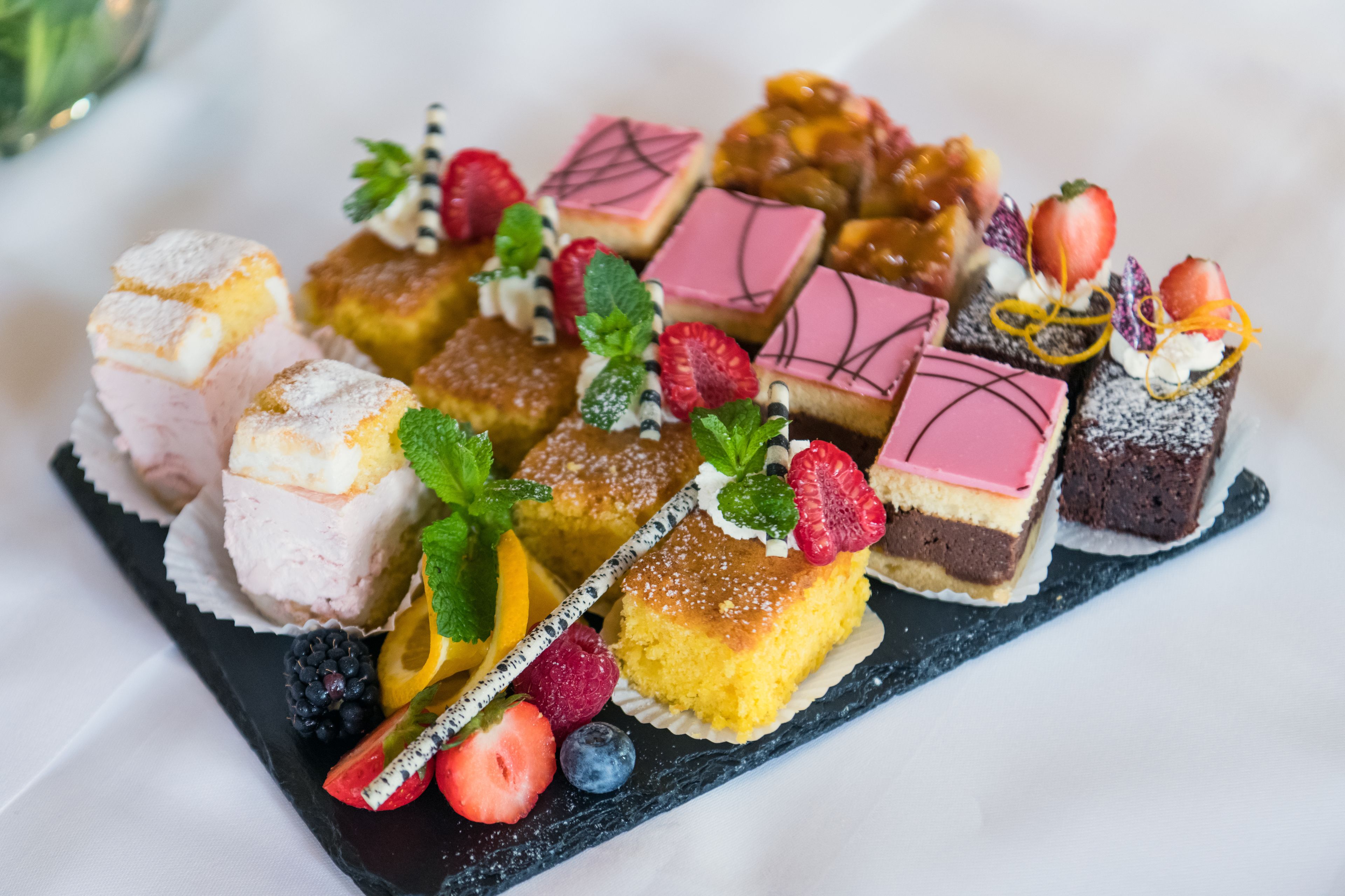 A variety of desserts arranged on a black slate board, including cakes and pastries with fruit garnishes.