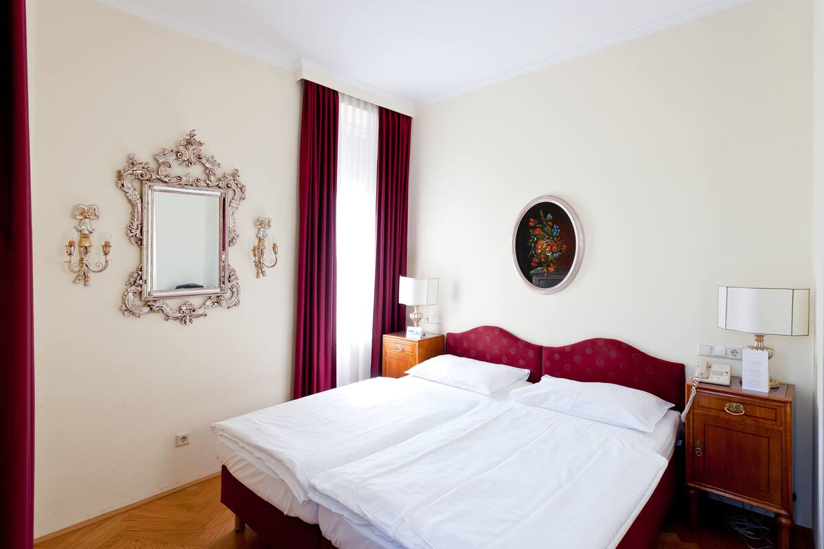 Een hotelkamer met een groot bed, een nachtkastje met lamp, een spiegel en een schilderij aan de muur.
