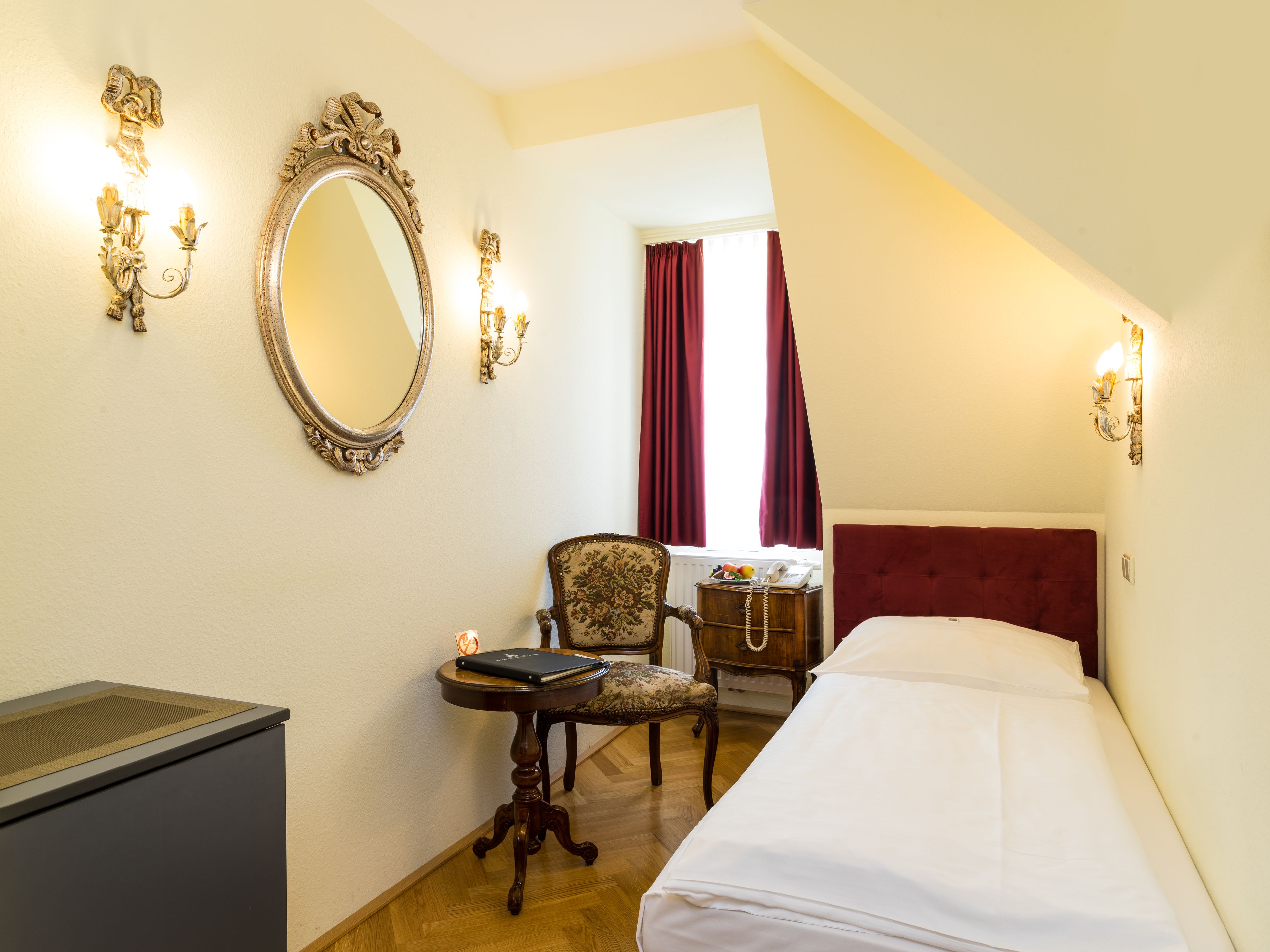 Ein Hotelzimmer mit Bett, Schreibtisch, Stuhl, Kommode, Spiegel und Wandleuchten.