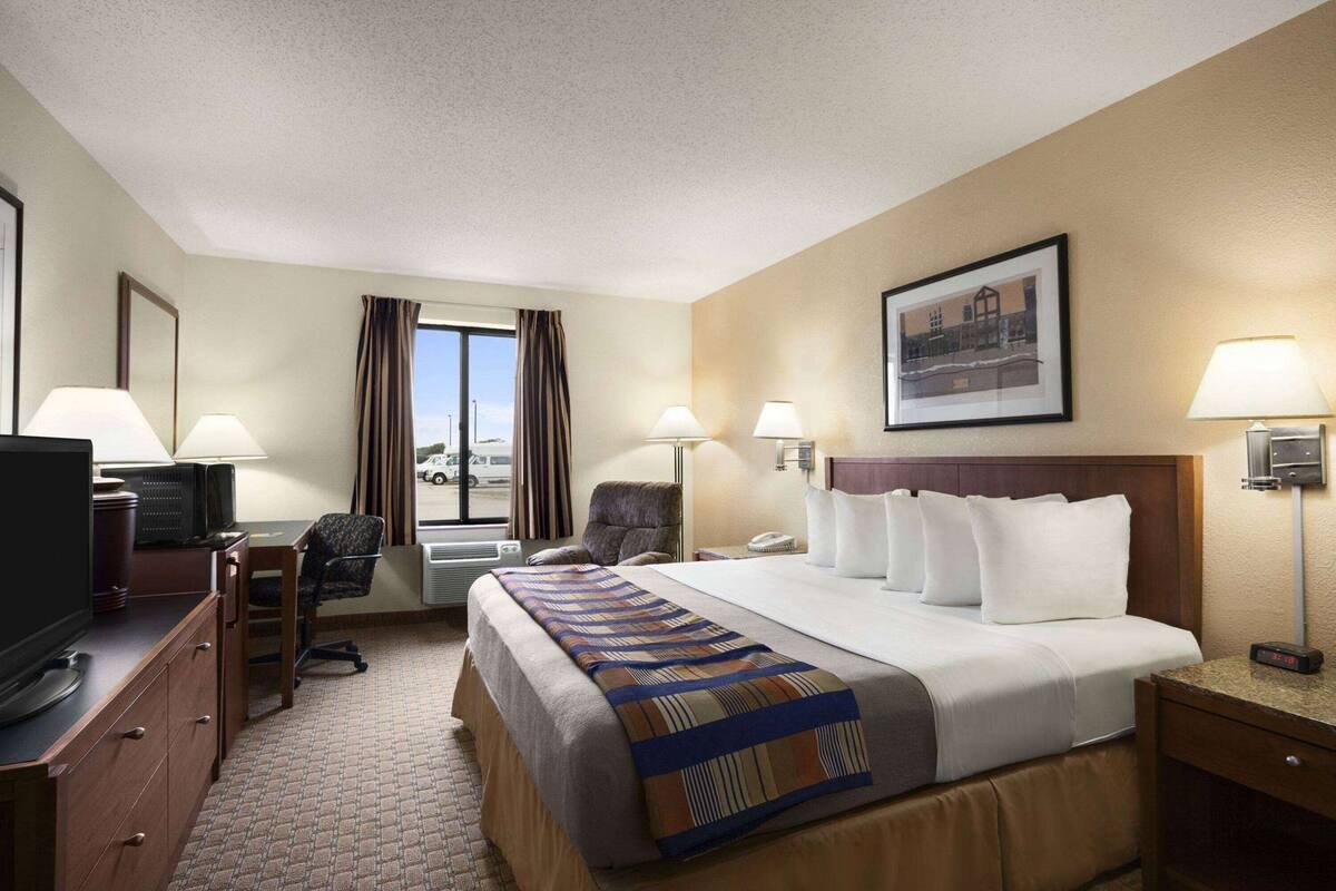 Habitación de hotel con cama, escritorio, televisión, lámparas y ventana con cortinas.