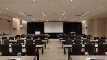 A conference room with rows of tables and chairs, a projector screen, and a stage with a podium.