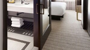 A hotel room with a bed, a bathroom with a sink and mirror, and a view of the outside through the window. - The Clift Royal Sonesta San Francisco (San Francisco)