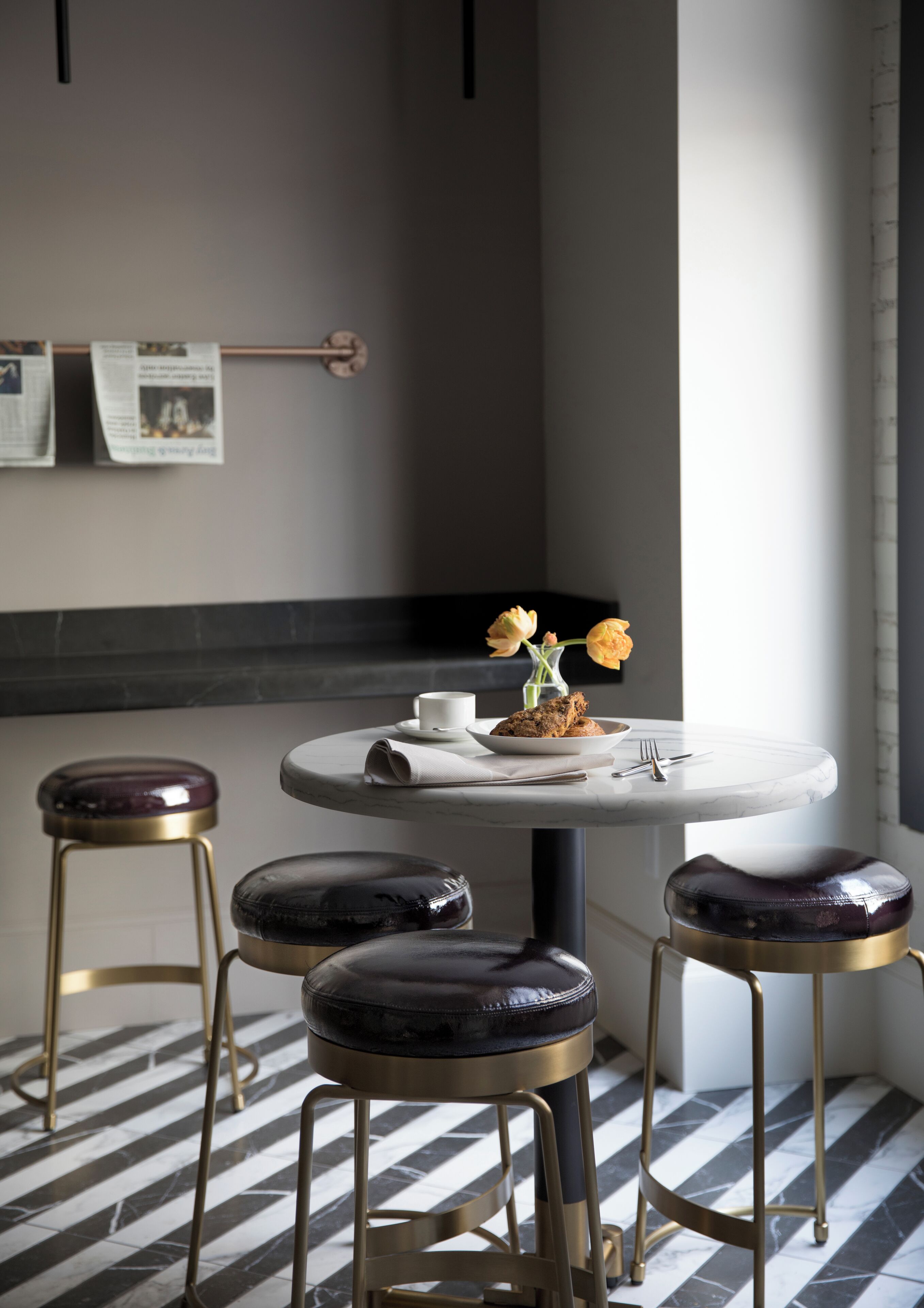 Een moderne bar met een ronde tafel, twee krukken en een vaas met gele bloemen.