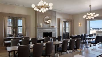 A conference room with multiple tables and chairs, a fireplace, and large windows offering a view.