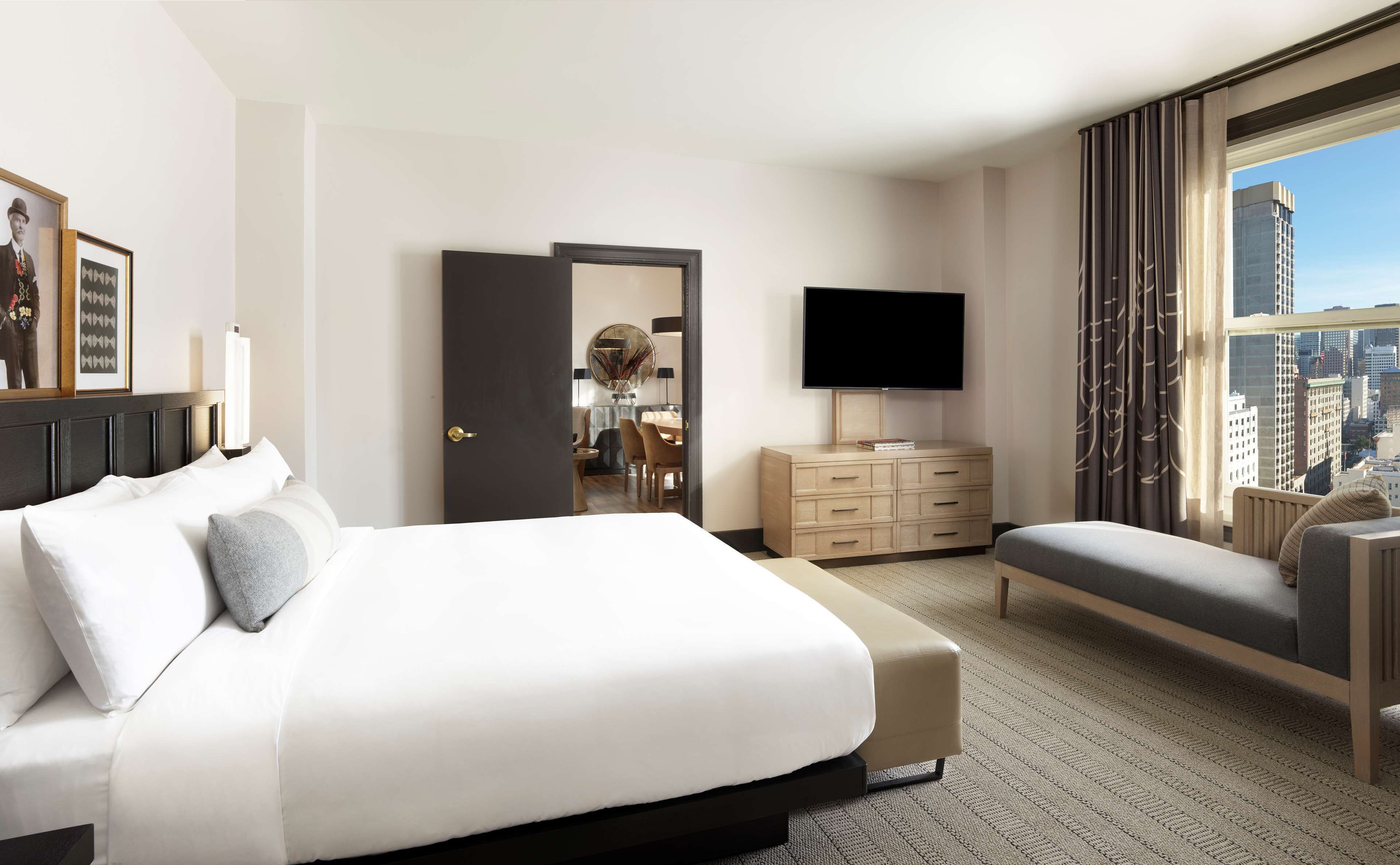 A hotel room with a large bed, a TV, a desk, and a view of the city.