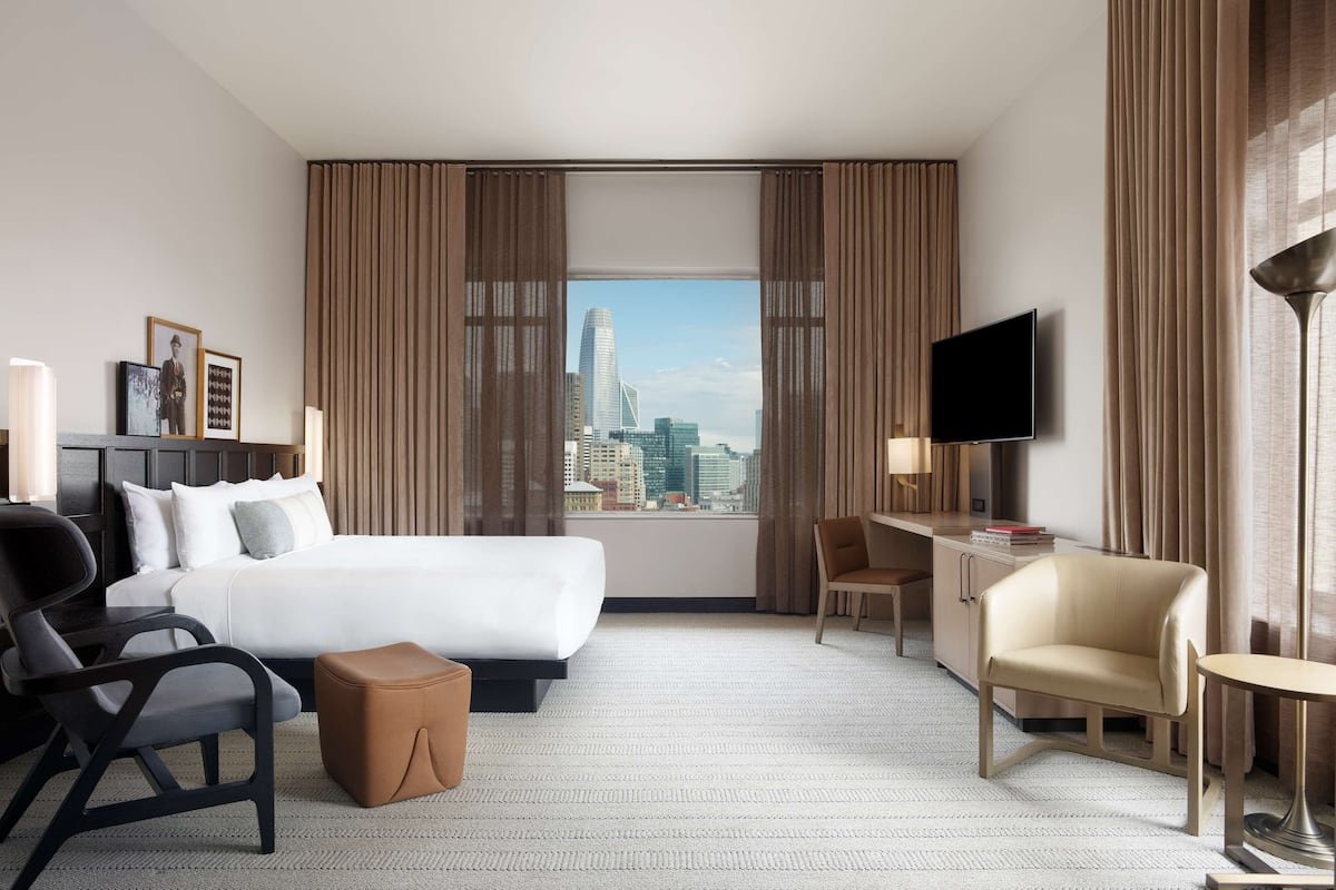 Une chambre d’hôtel avec un grand lit, un bureau, une chaise, une télévision et une vue sur les toits de la ville.