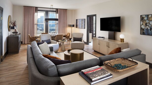A modern hotel room with a grey sofa, a dining table, a TV, and a large window with curtains. - The Clift Royal Sonesta San Francisco (San Francisco)