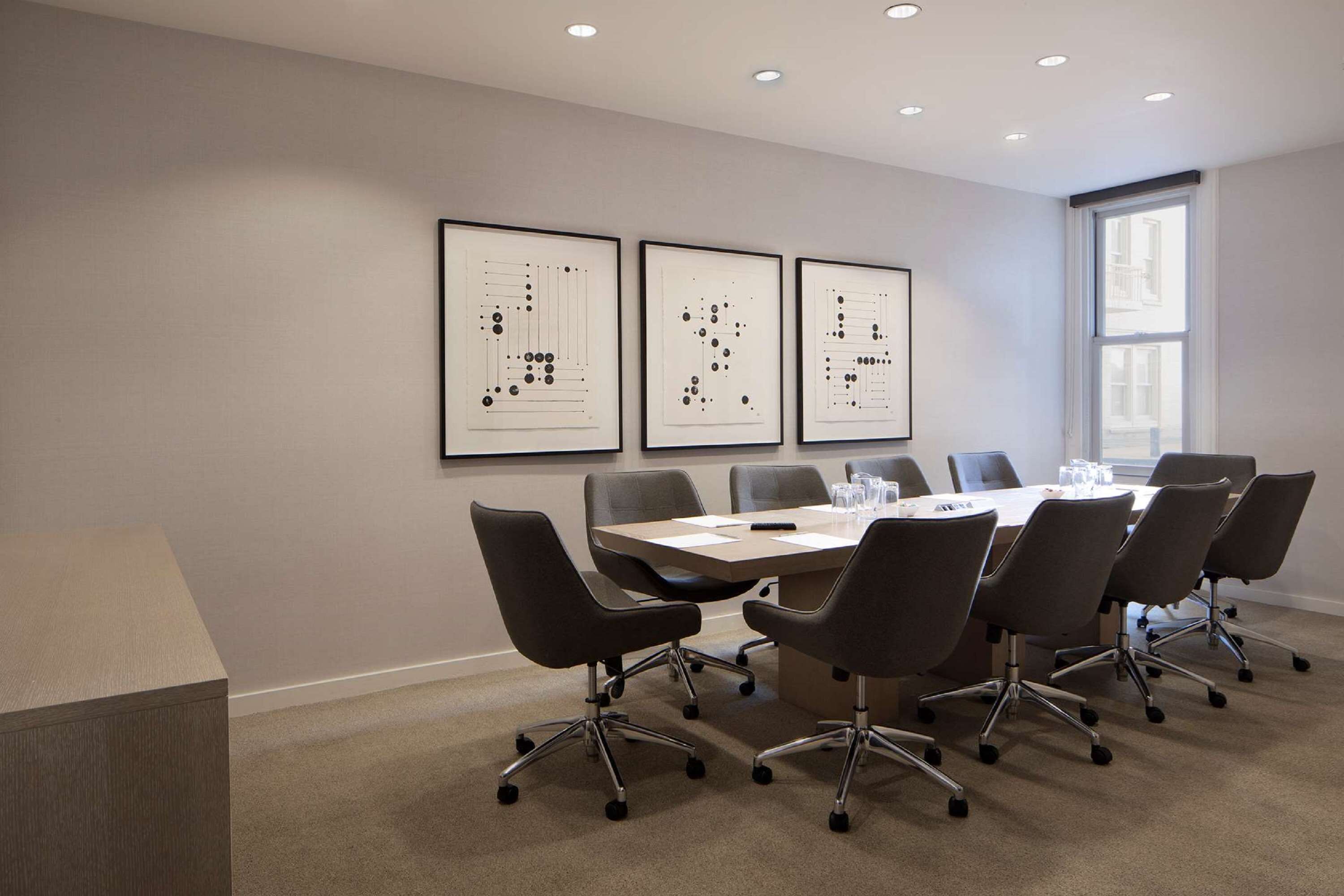Une salle de conférence avec une longue table, six chaises et trois œuvres d’art abstraites encadrées accrochées au mur.
