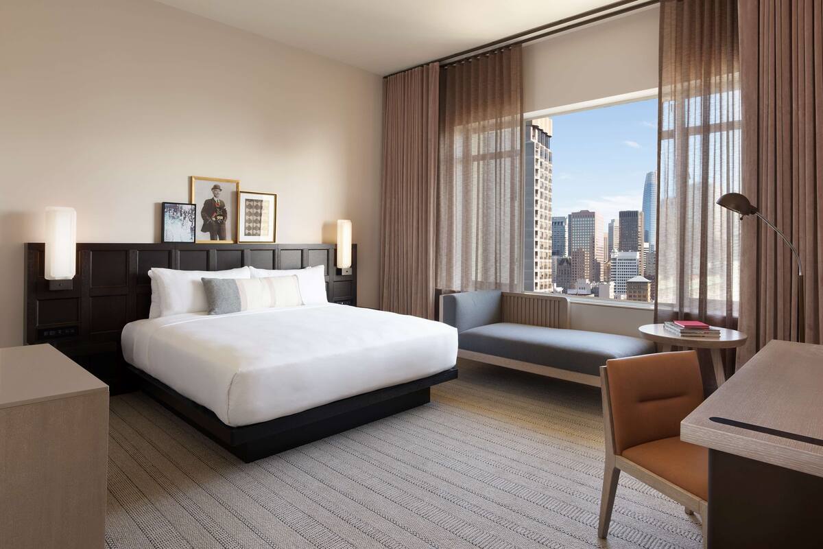 Une chambre d’hôtel dotée d’un grand lit, d’un coin salon, d’un bureau et offrant une vue sur la ville.