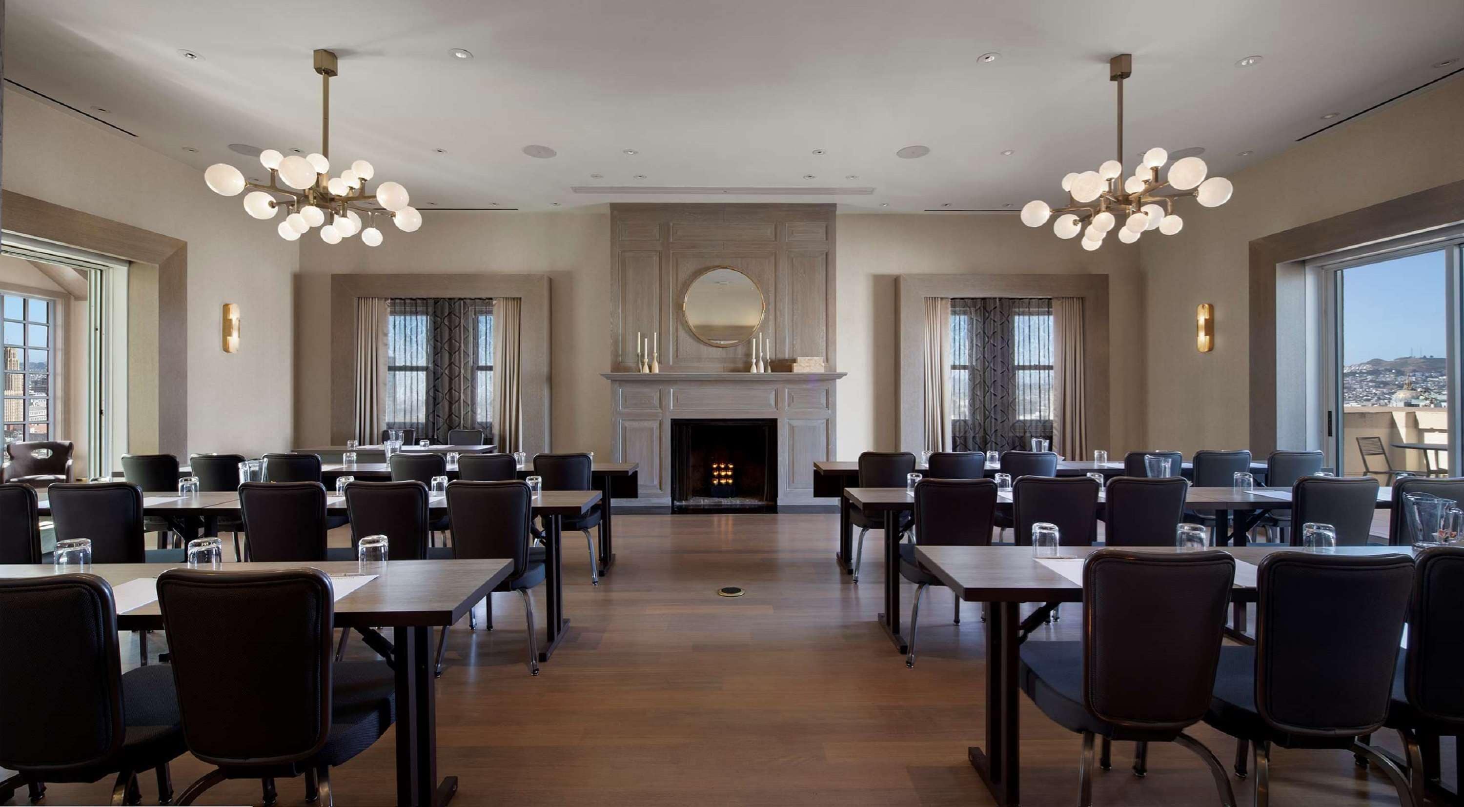 Un vaste espace dédié à la salle à manger, avec de nombreuses tables et chaises, une cheminée et de grandes fenêtres offrant une vue sur la ville.