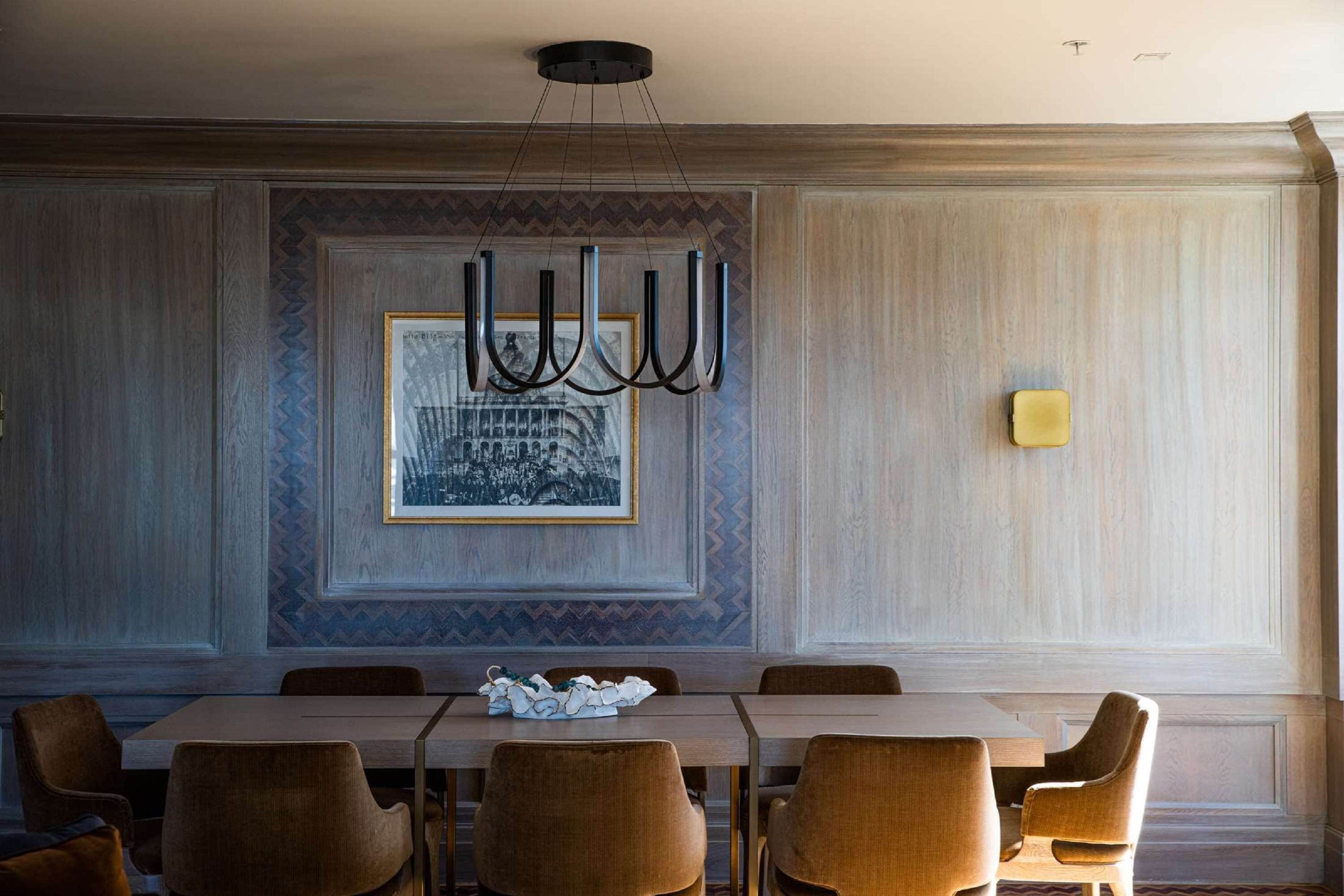 Un espace repas comprenant une grande table et plusieurs chaises, un lustre et un tableau encadré accroché au mur.