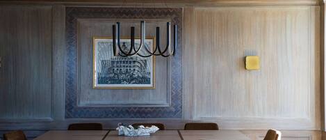 Un espace repas comprenant une grande table et plusieurs chaises, un lustre et un tableau encadré accroché au mur.