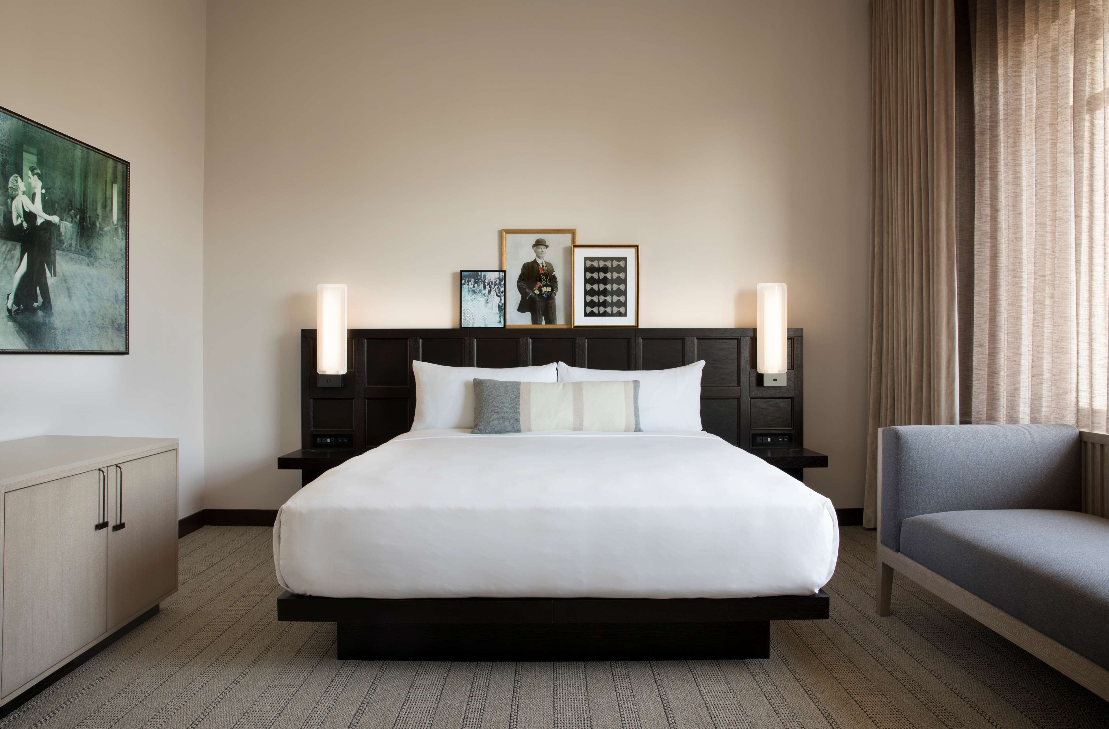 Una habitación de hotel con una cama grande, mesitas de noche, una silla y obras de arte en las paredes.