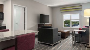 Una habitación de hotel moderna con kitchenette, televisión de pantalla plana, ventana grande con vistas y zona de estar con sofá y sillones.