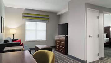 Hotelkamer met een bank, een kleine tafel, een televisie op een dressoir en een deur naar een andere kamer.