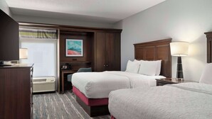 Habitación de hotel con dos camas, un escritorio, una silla, una lámpara y un cuadro en la pared.