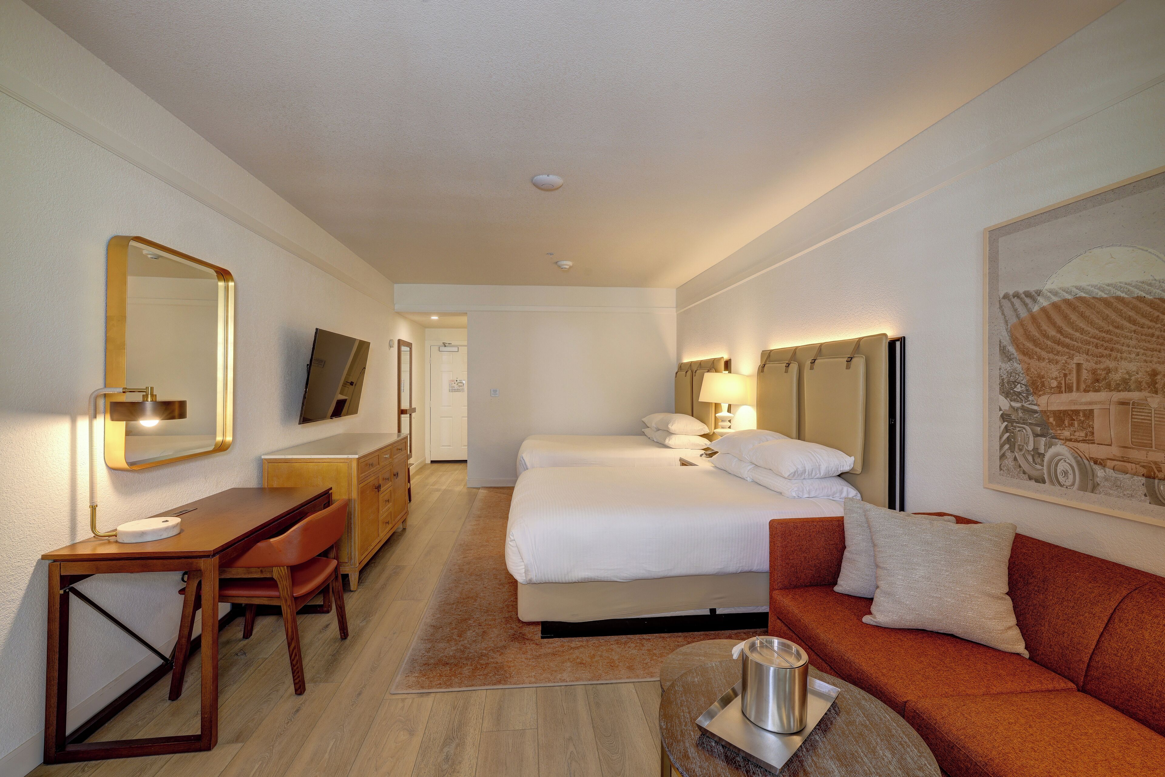 A hotel room with a bed, a desk, a chair, a sofa, a coffee table, and a painting on the wall.