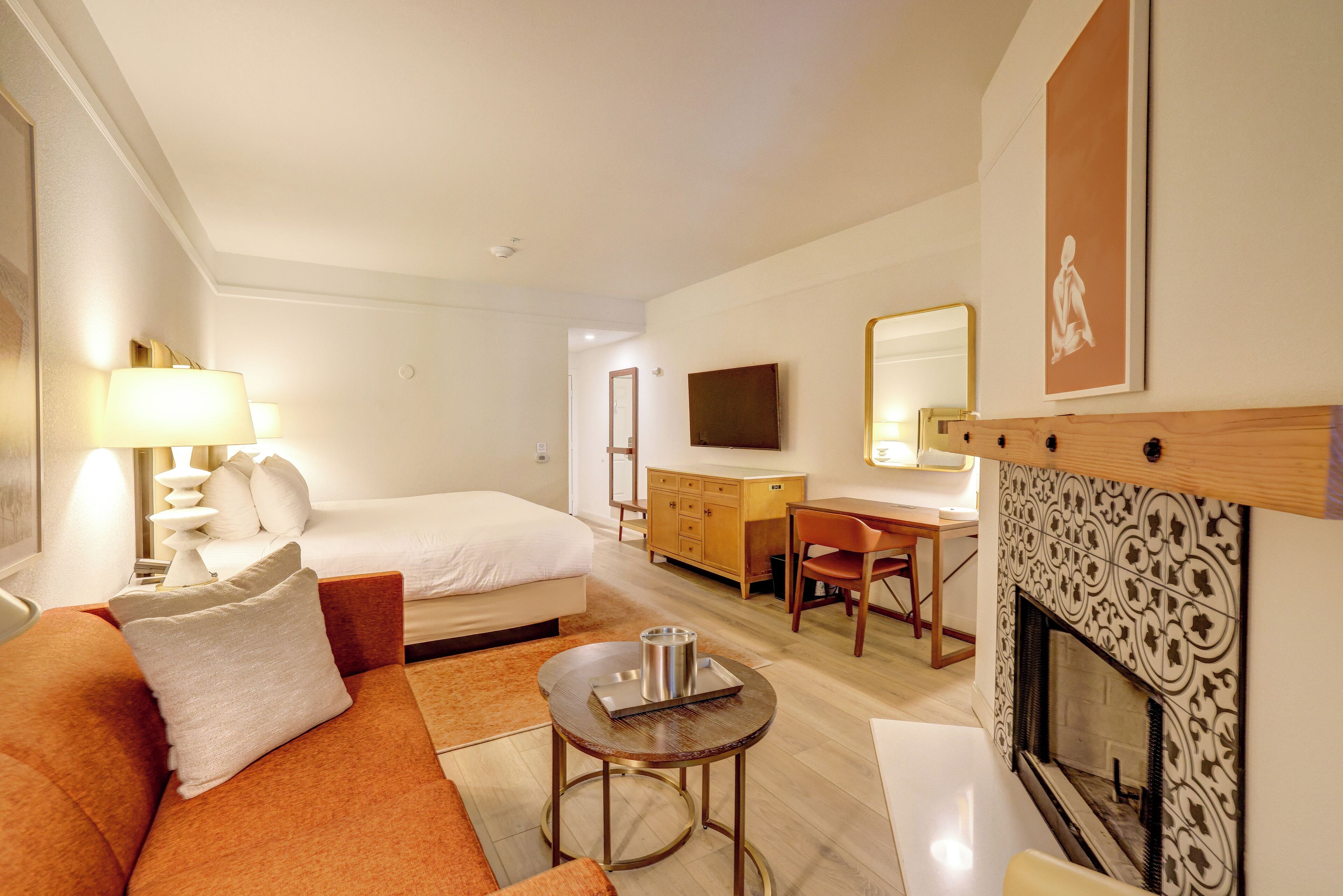A hotel room with a bed, a sofa, a desk, a television, and a fireplace.