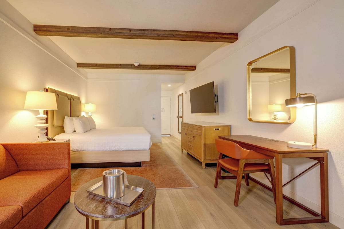 Habitación de hotel con cama, escritorio de madera, silla, sofá y televisor.