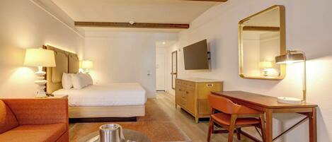 A hotel room with a bed, a wooden desk, a chair, a sofa, and a television.