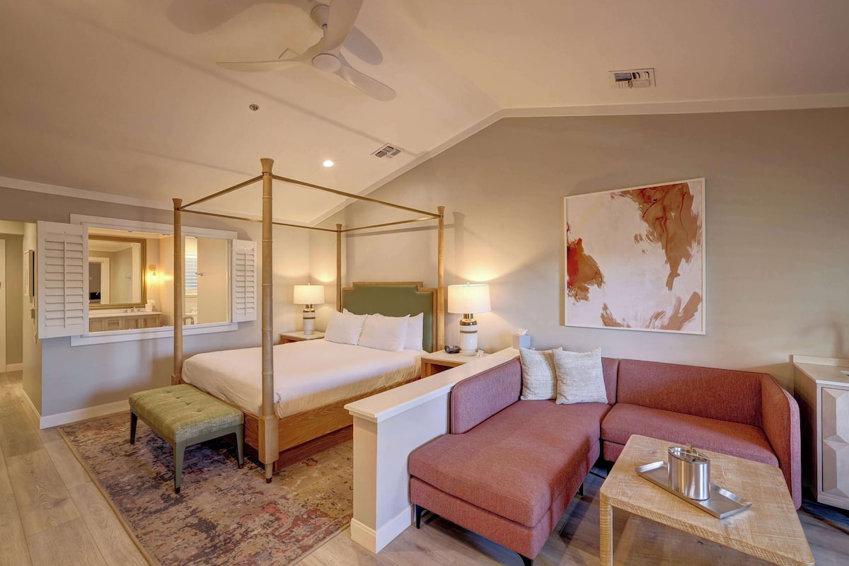 Habitación de hotel con cama con dosel, sofá, una mesita y un cuadro en la pared.