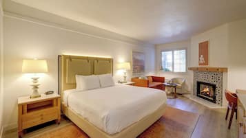 A hotel room with a large bed, bedside lamps, a fireplace, and a seating area with a chair and table.