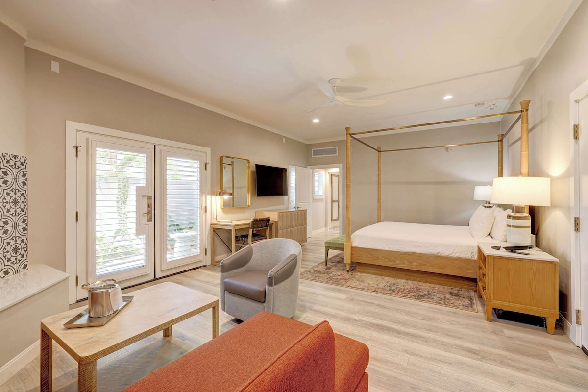 Una habitación de hotel con una cama con dosel, un escritorio con una silla, un televisor y una mesita de noche con una lámpara.