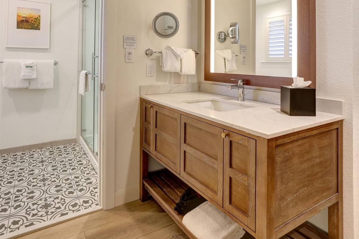 Un baño con tocador de madera, un espejo grande y cabina de ducha de vidrio.