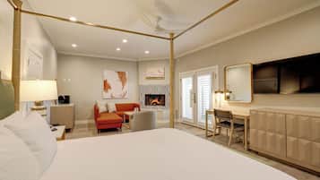 Une chambre d’hôtel avec un grand lit, un bureau, une chaise, un canapé, une cheminée et un téléviseur.
