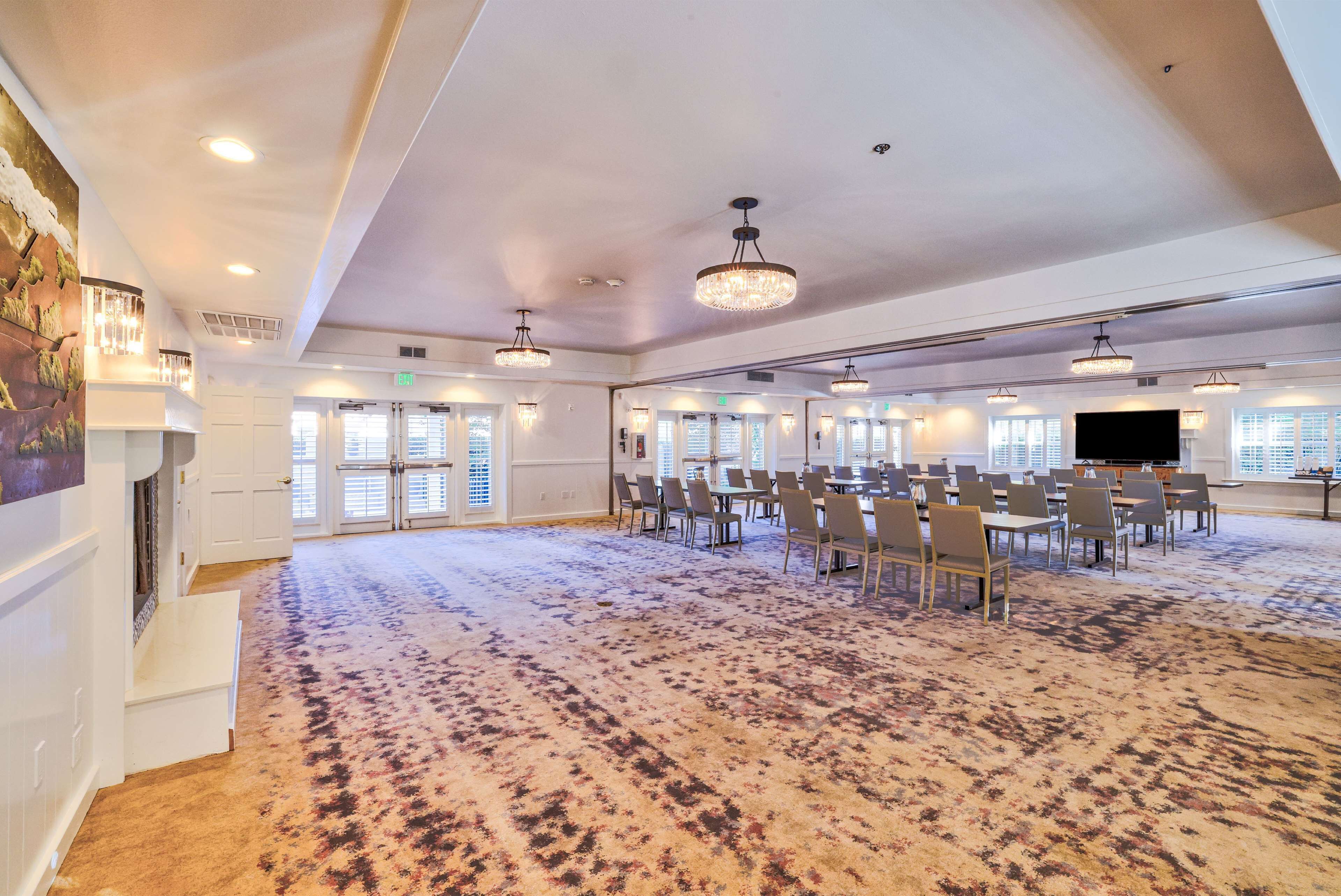 Une grande salle de conférence dotée d’un tapis à motifs, de nombreuses tables et chaises, ainsi que d’un éclairage au plafond.
