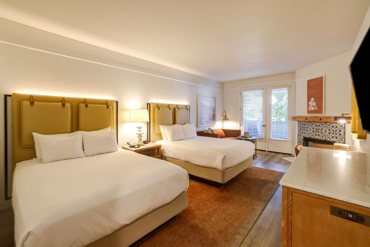 Une chambre d’hôtel avec deux lits, une petite kitchenette, une salle de bain avec douche et une porte donnant sur un balcon.