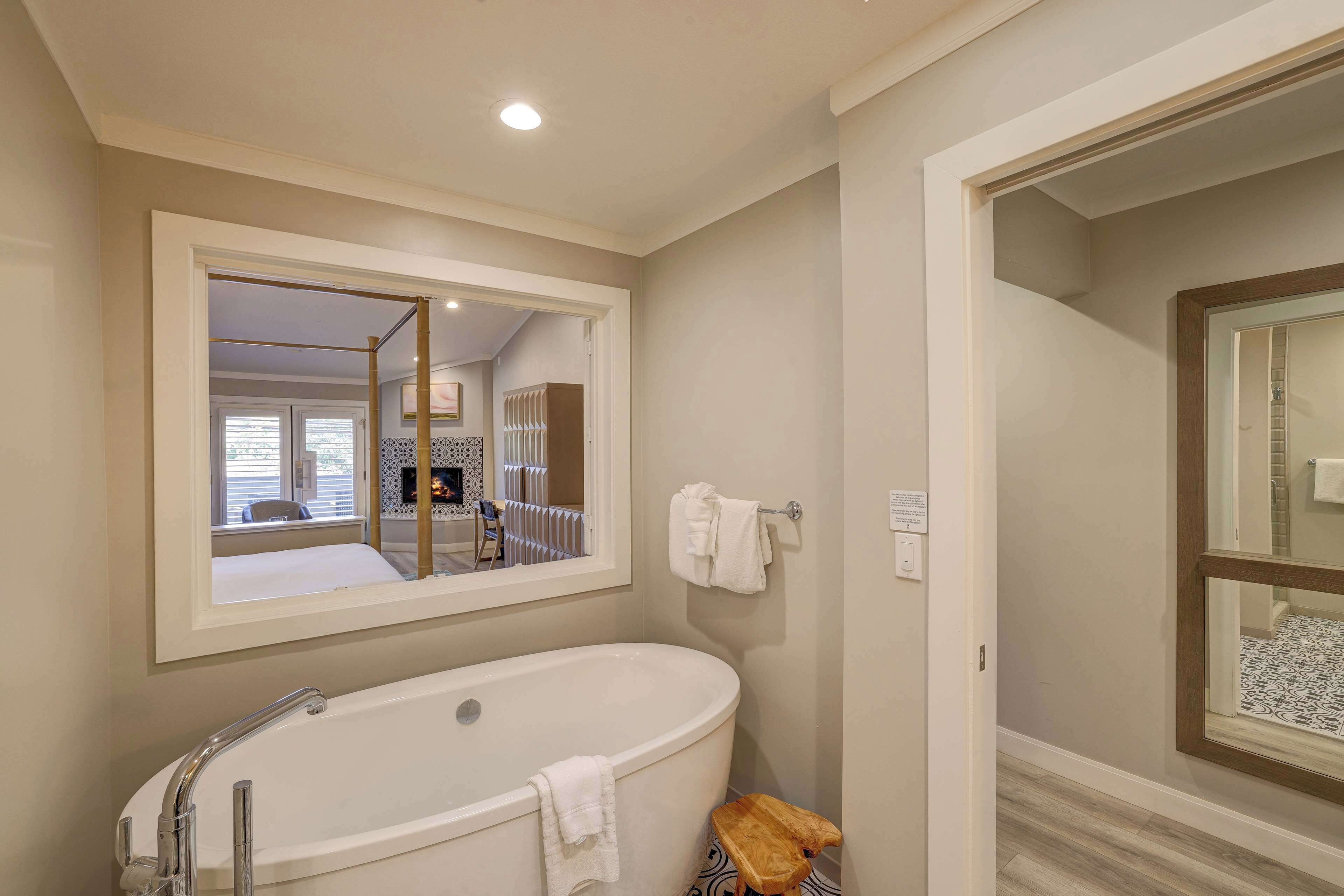 Un baño con una bañera independiente, un espejo grande y un taburete de madera.