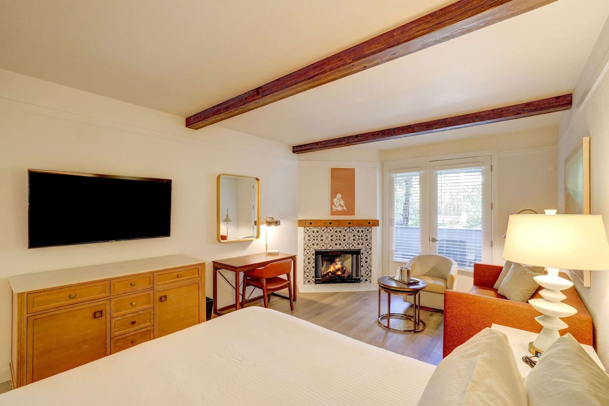 Habitación de hotel con cama, escritorio, silla, chimenea, televisor y sofá.