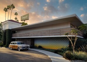Un hotel moderno con una estructura de dos pisos, un estacionamiento cubierto y un coche clásico estacionado frente a él.