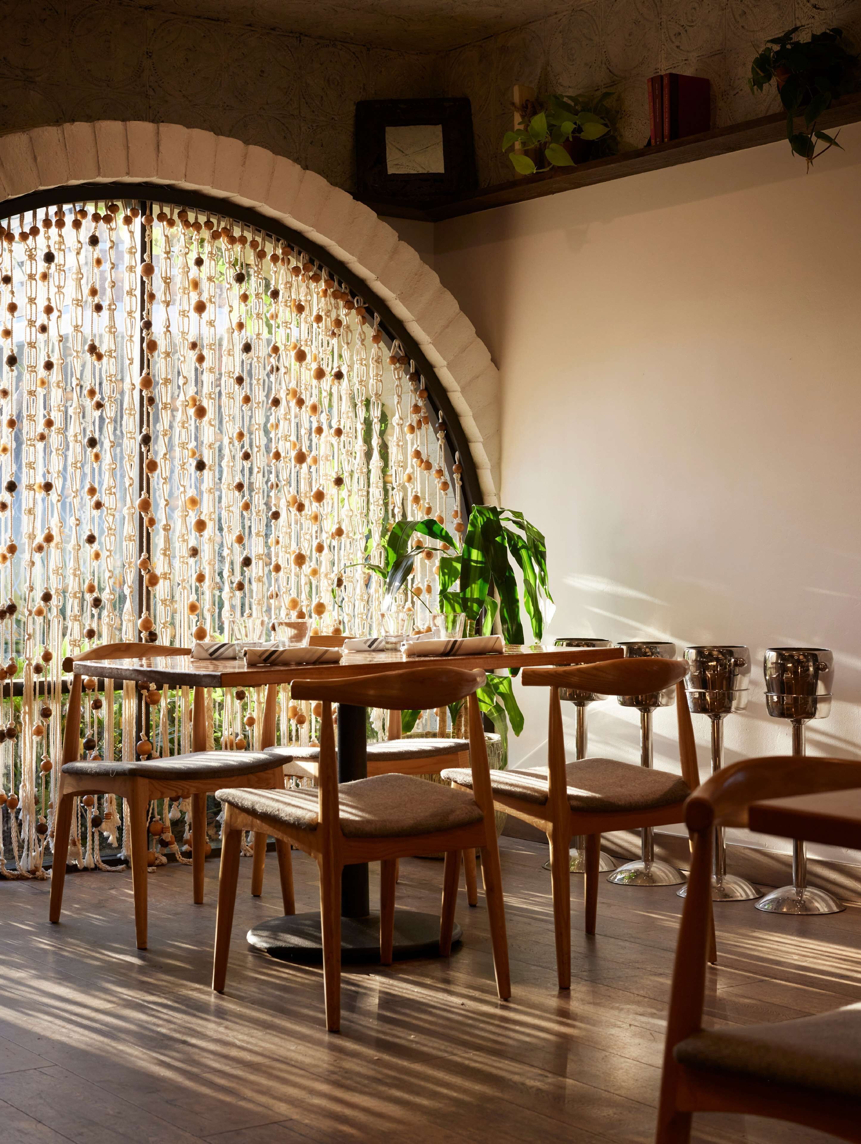 Un comedor con mobiliario de madera, un amplio ventanal de arco y una planta en maceta.