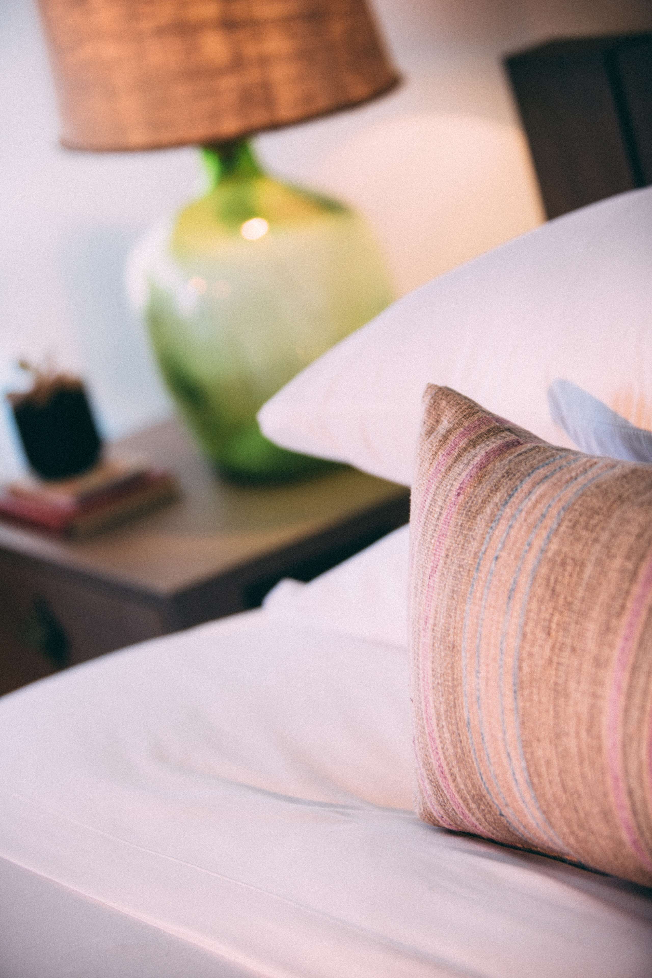 A neatly made bed with a striped pillow and a green lamp on a bedside table.