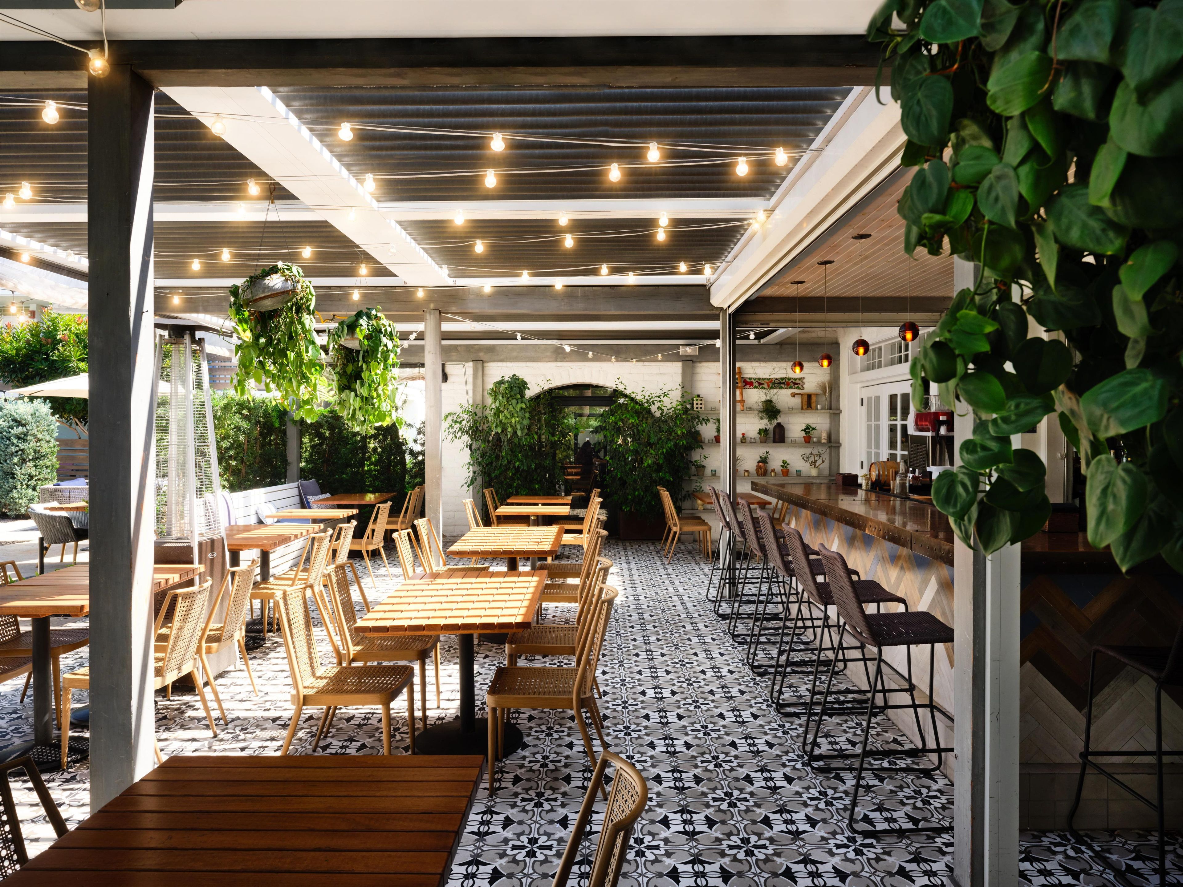 An indoor dining area with wooden tables and chairs, a patterned floor, and hanging plants.
