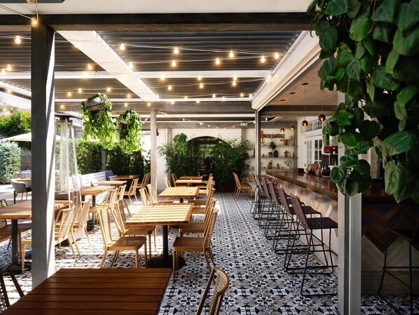 An indoor dining area with wooden tables and chairs, a patterned floor, and hanging plants.