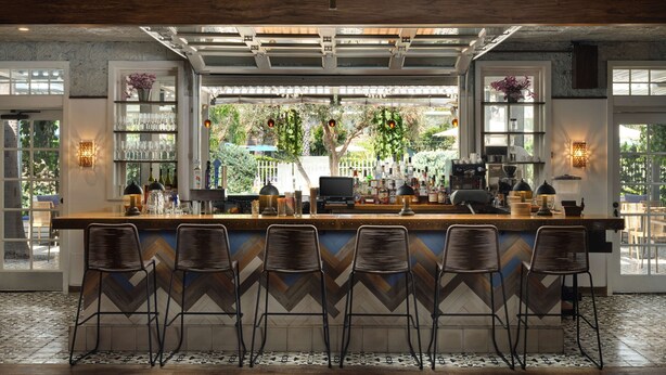 Zona de bar con una barra alargada, varios taburetes y vistas al exterior a través de amplios ventanales.