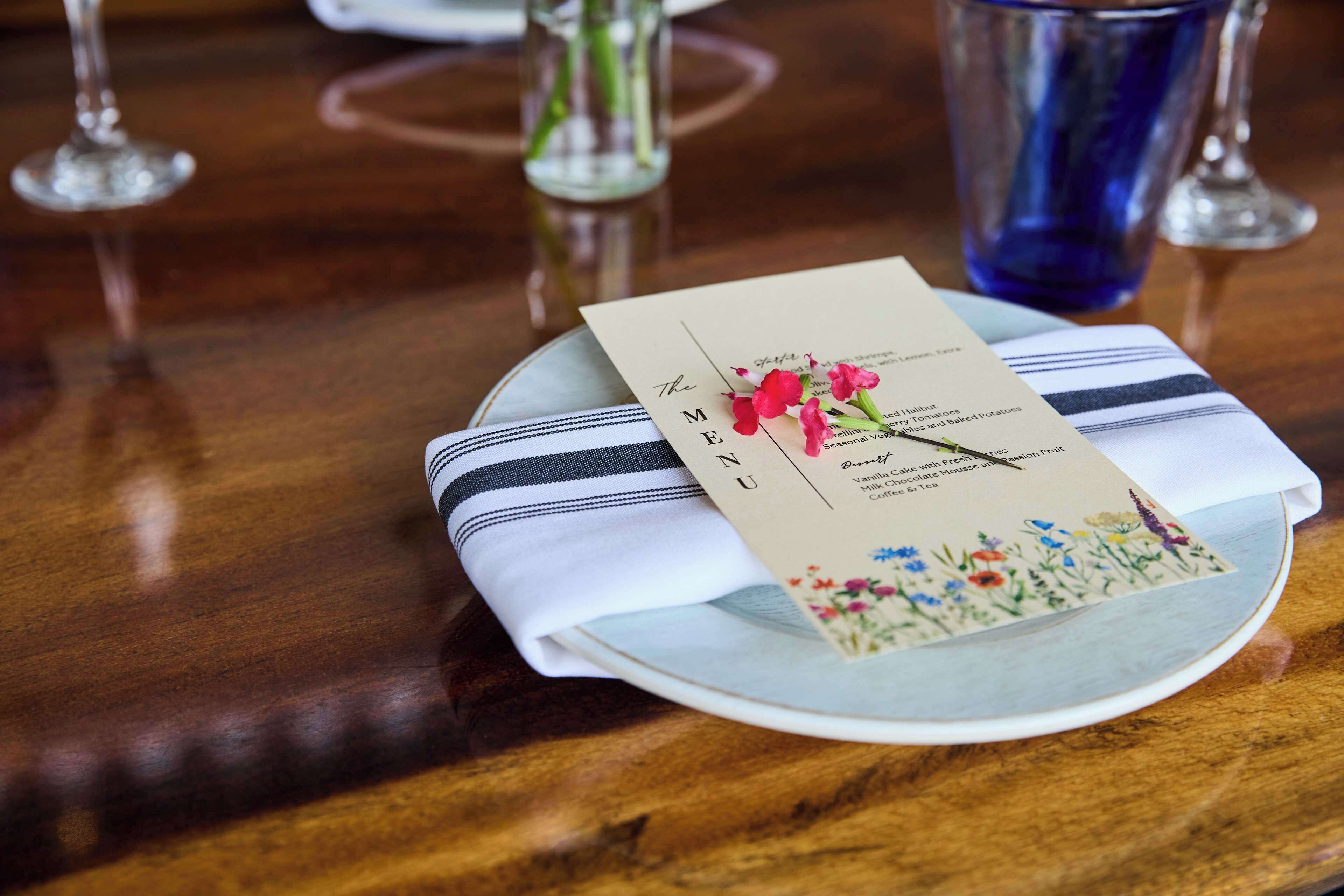 Een gedekte tafel met een menukaart op een bord, een gestreepte servet en een glas water.