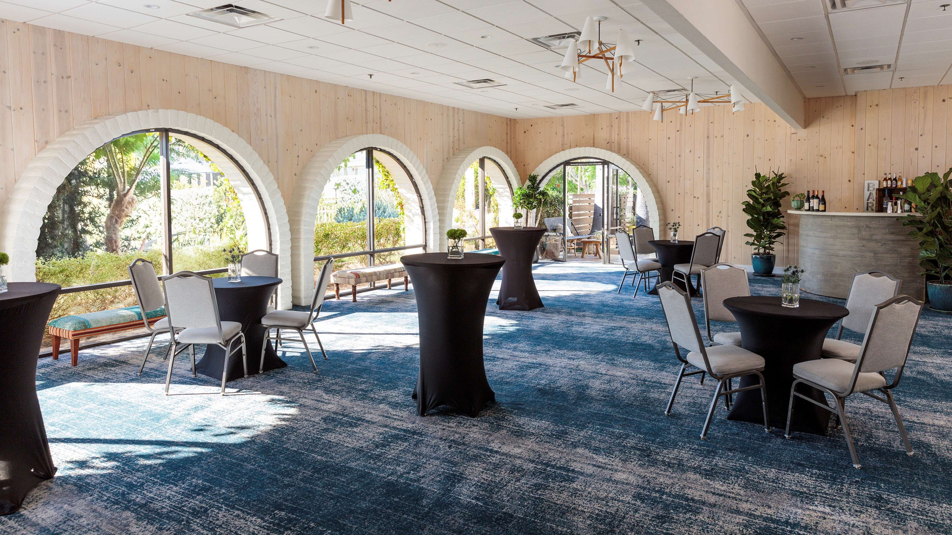 A spacious indoor area with multiple tables and chairs, large arched windows, and a wooden wall.
