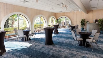 A spacious indoor area with multiple tables and chairs, large arched windows, and a wooden wall.