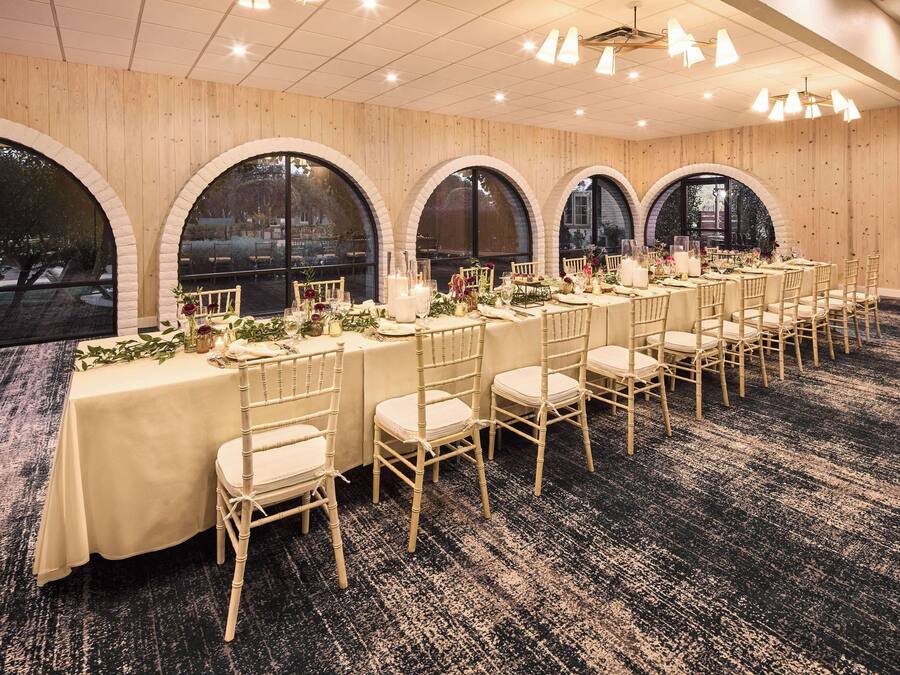 A banquet hall with long tables set for events, wooden paneled walls, and large arched windows.