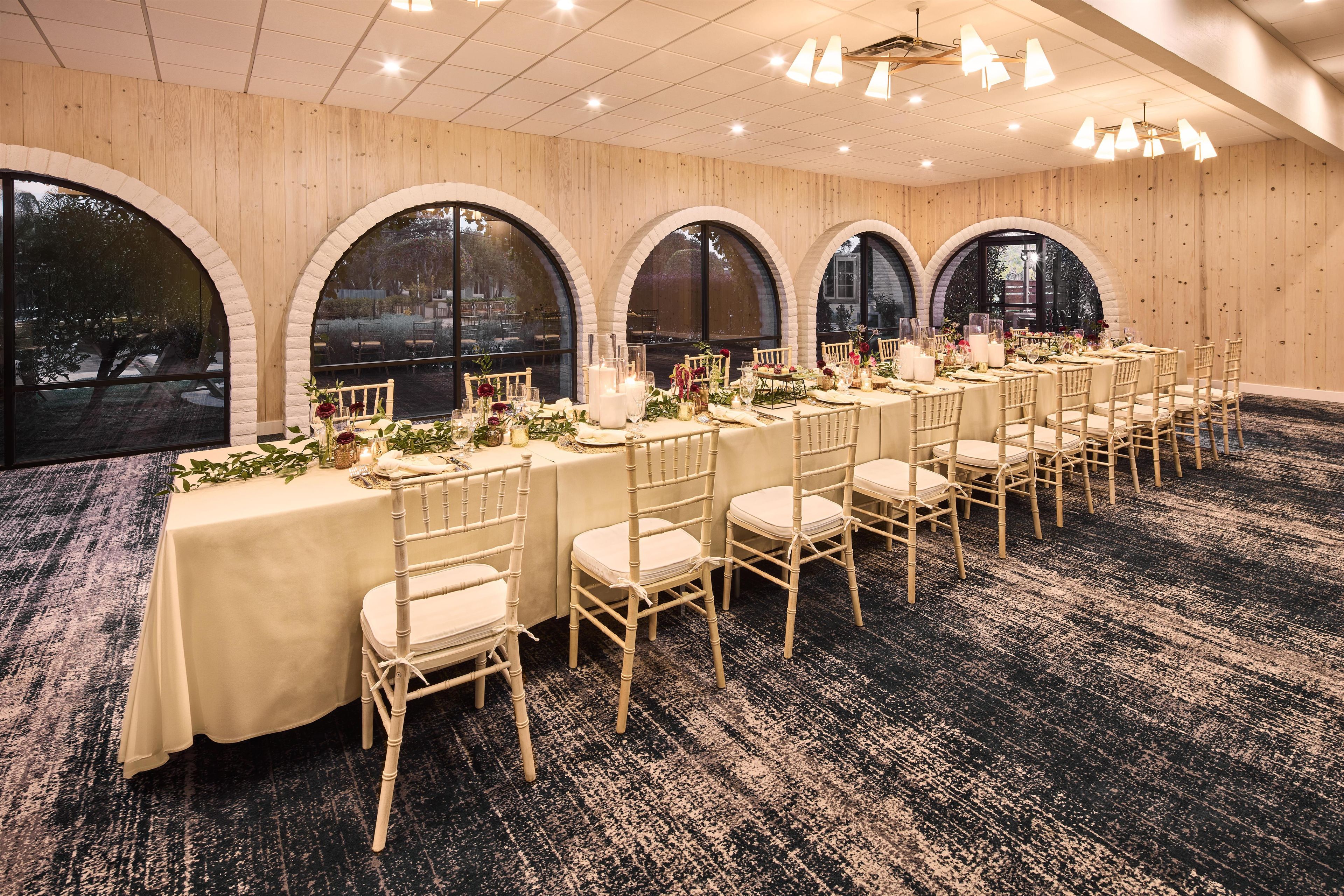 Een balzaal met meerdere gedekte tafels voor een formeel evenement, met witte tafelkleden, kristal en bloemstukken.