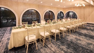 Een balzaal met meerdere gedekte tafels voor een formeel evenement, met witte tafelkleden, kristal en bloemstukken.