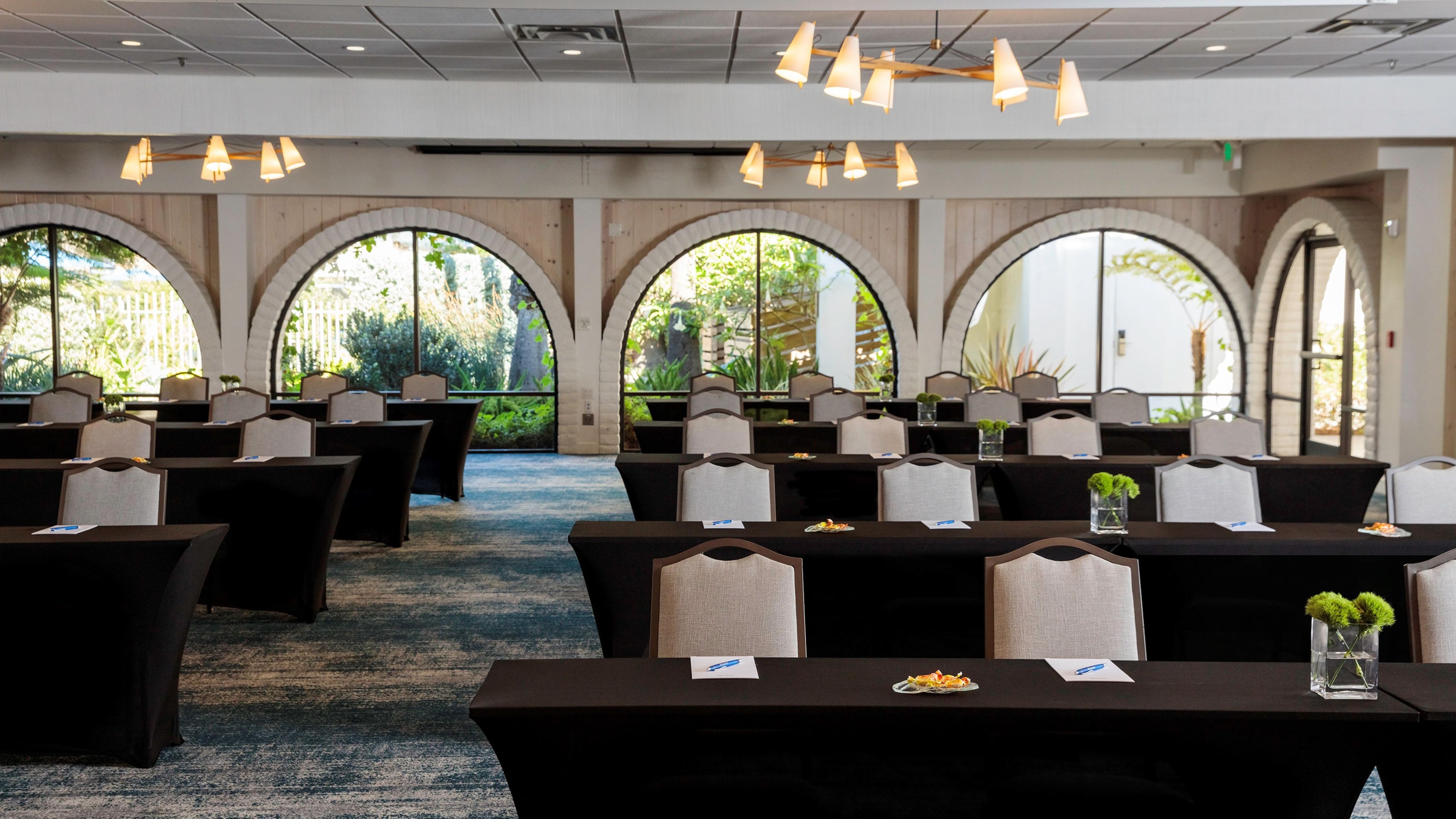 A conference room with tables and chairs, large arched windows, and hanging lights.