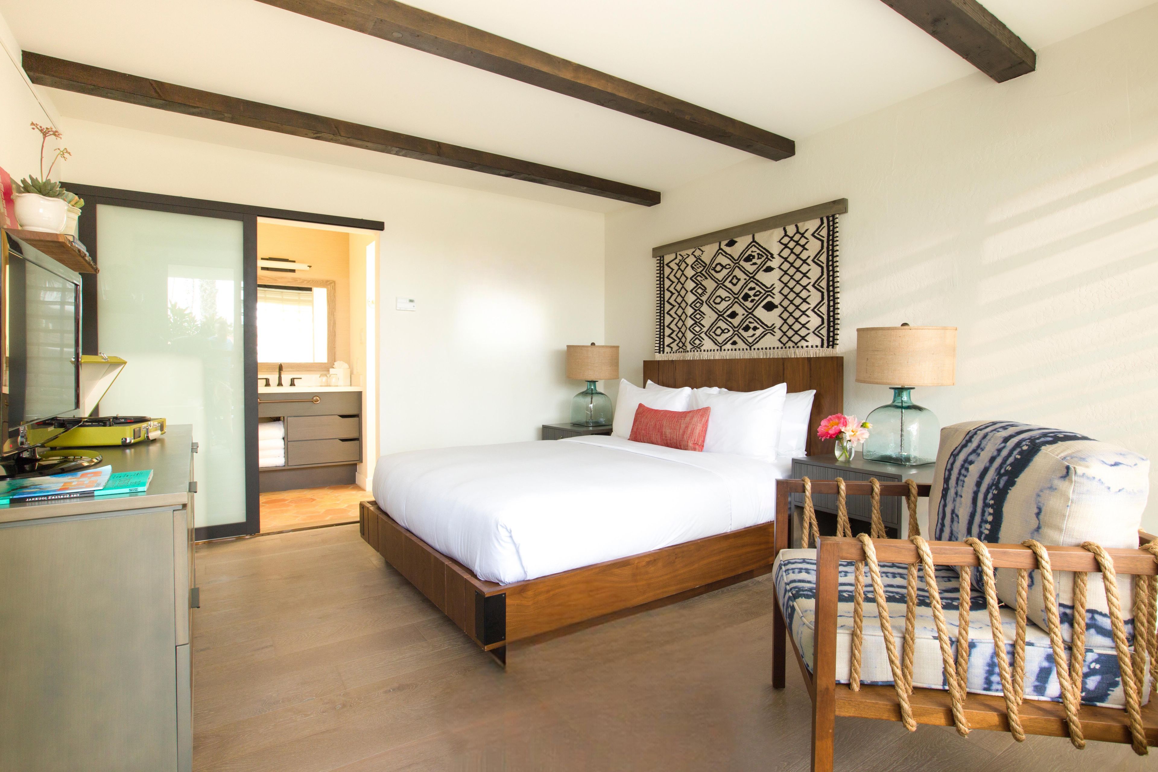 Une chambre à coucher avec un lit en bois, des tables de chevet, une chaise à dossier en corde et une décoration murale à motifs.